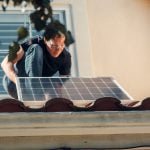 a man in black shirt installing a solar panel on the roof